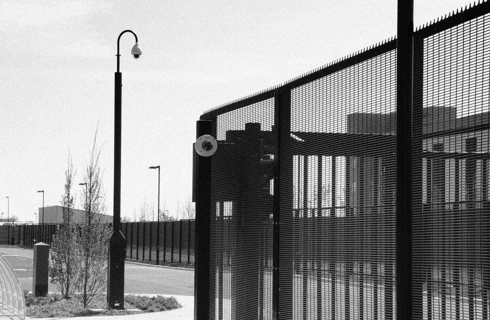 Security cameras mounted on a pole and on a high-security perimeter fence